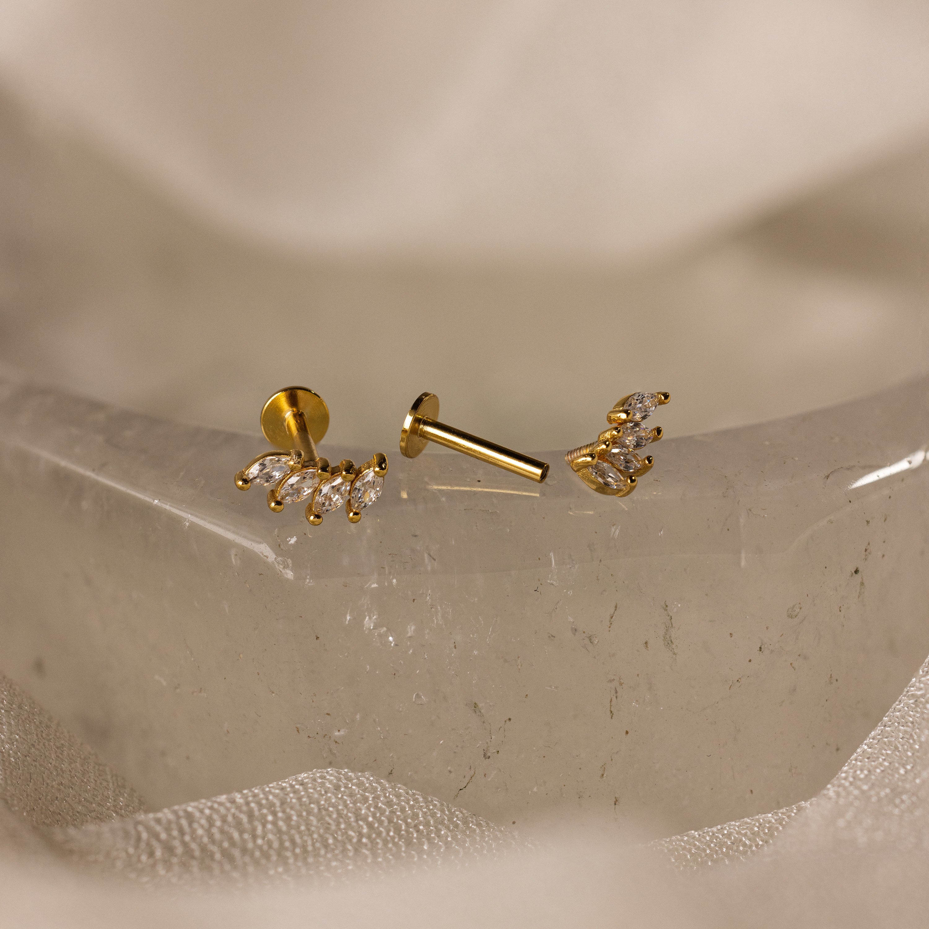 Gold stud earrings with small clear stones, shown on a crystal surface—ideal as wedding jewelry or styled with Marquise Diamond Climbers for extra elegance.