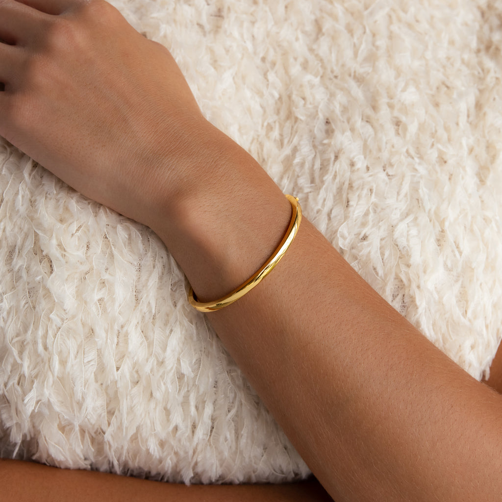 A hand with the Classic Bangle rests on a textured white pillow, highlighting this timeless, minimalist piece of jewelry.