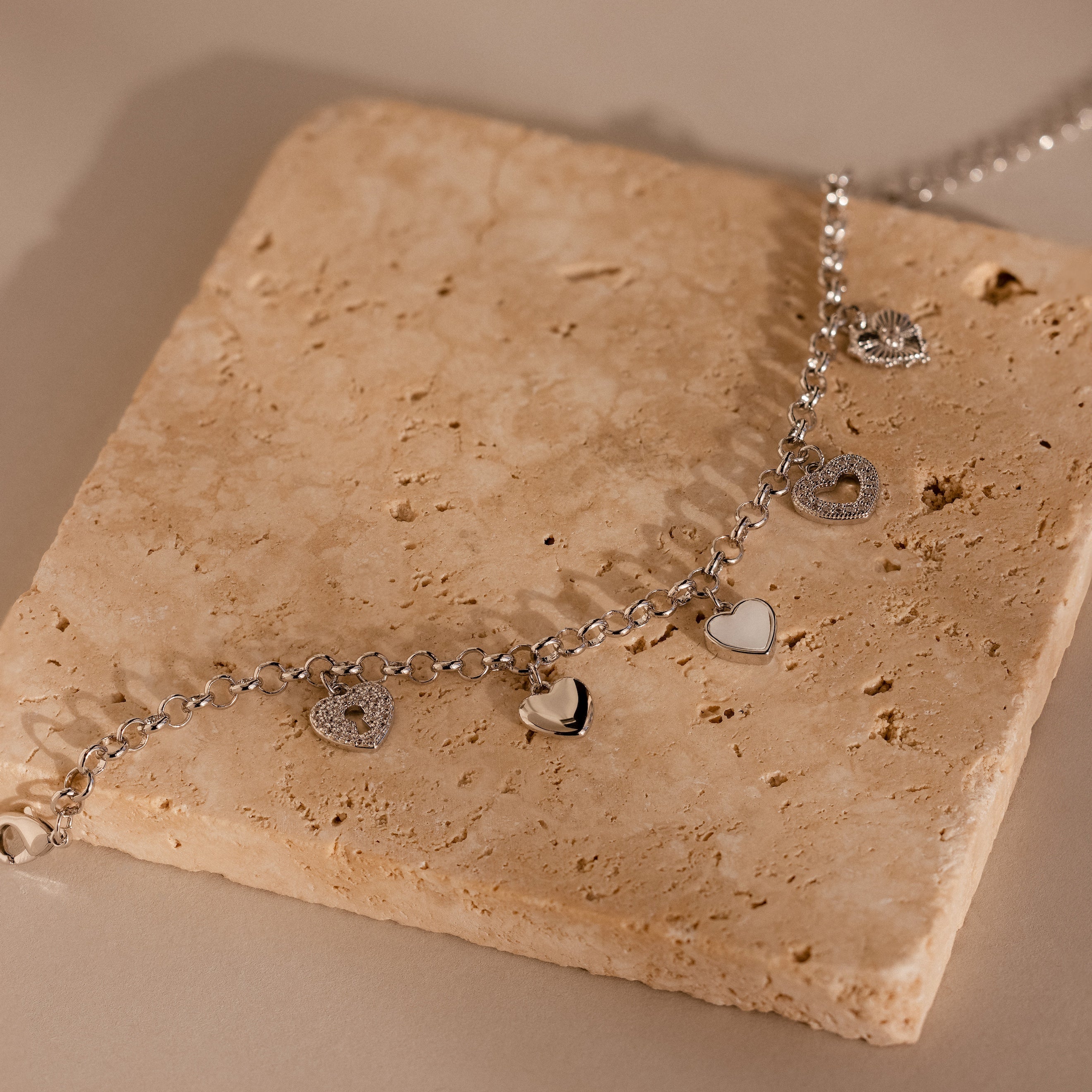 Heart Charm Bracelet in Sterling Silver, featuring delicate heart charms and displayed on a textured beige stone—a thoughtful gift for your girlfriend.