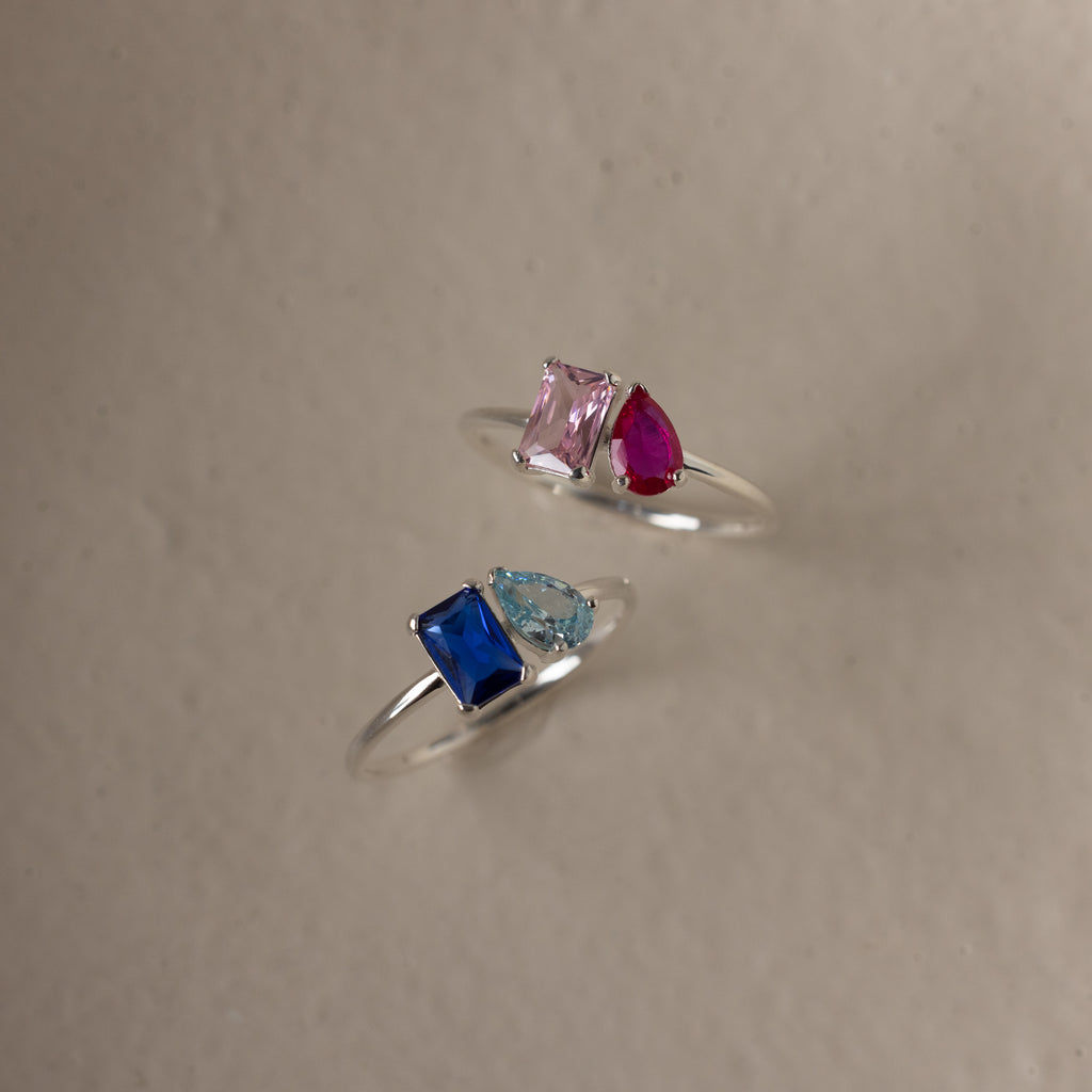 The Toi et Moi Birthstone Ring in Sterling Silver features two colorful gemstones on a light, textured surface—perfect as a customizable gift or unique Christmas present.