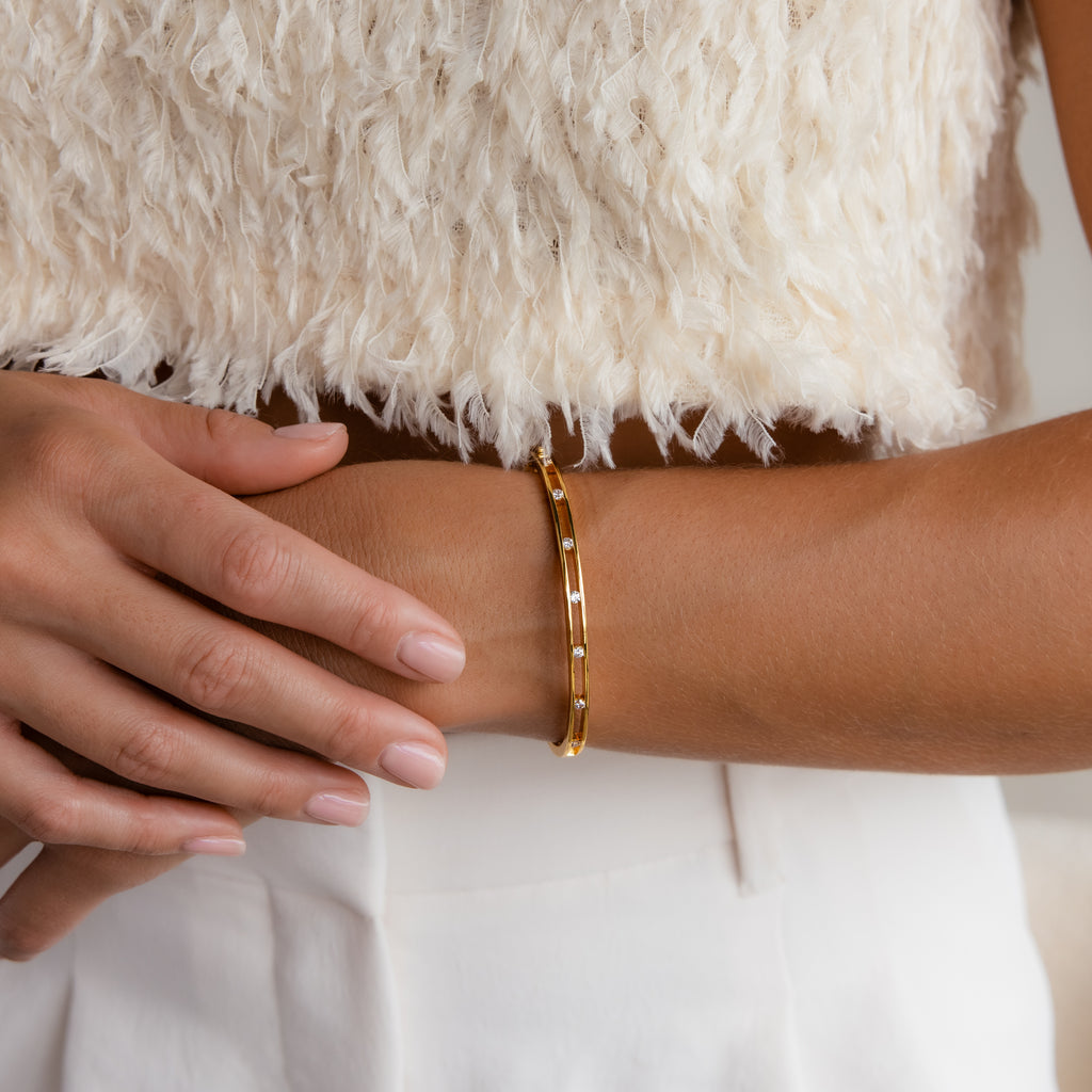 A woman wears a Lace Diamond Bangle in Sterling Silver with an open station design, paired with a cream textured top and white pants, her hands gently crossed.