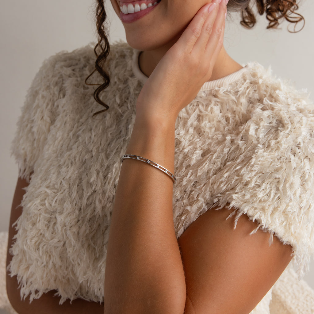 Woman in a textured cream top smiling, wearing the Lace Diamond Bangle in Sterling Silver with an open station design, and touching her face with one hand.