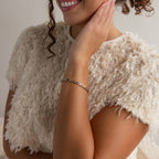 Woman in a textured cream top smiling, wearing the Lace Diamond Bangle in Sterling Silver with an open station design, and touching her face with one hand.