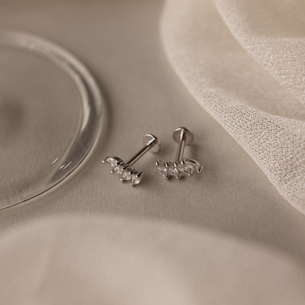 The Marquise Diamond Climbers in Silver—elegant stud earrings with sparkling stones, ideal for wedding jewelry—are showcased on a light beige fabric background.