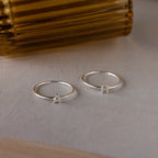 Two Alex Dainty Letter Rings, both featuring an "A," are displayed on a smooth surface next to a brown glass item—an ideal personalized jewelry choice for anyone who loves elegant initial rings.