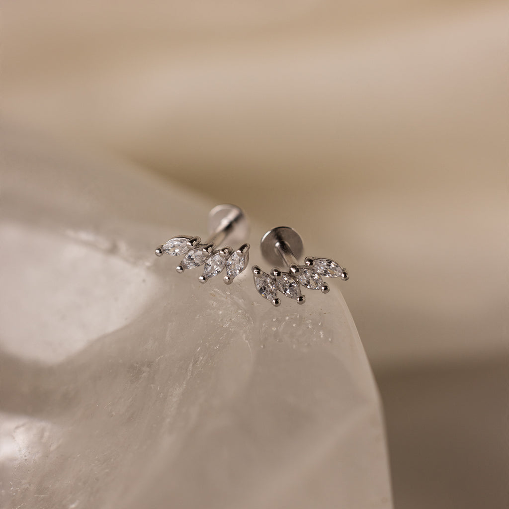 Marquise Diamond Climbers are silver stud earrings adorned with small, leaf-shaped crystals, capturing the elegance of wedding jewelry on a smooth, translucent surface.