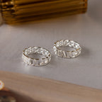 Two Newsletter Curb Name Rings in Sterling Silver, each with a unique engraved name, featuring chain design bands, are displayed on a neutral surface.