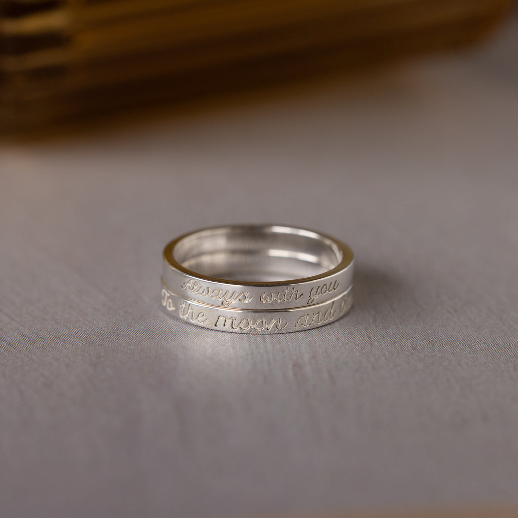 The Ann Thin Message Ring in Sterling Silver rests on a light surface—engraved with "Always with you to the moon and...", it’s a thoughtful message ring and perfect holiday gift.