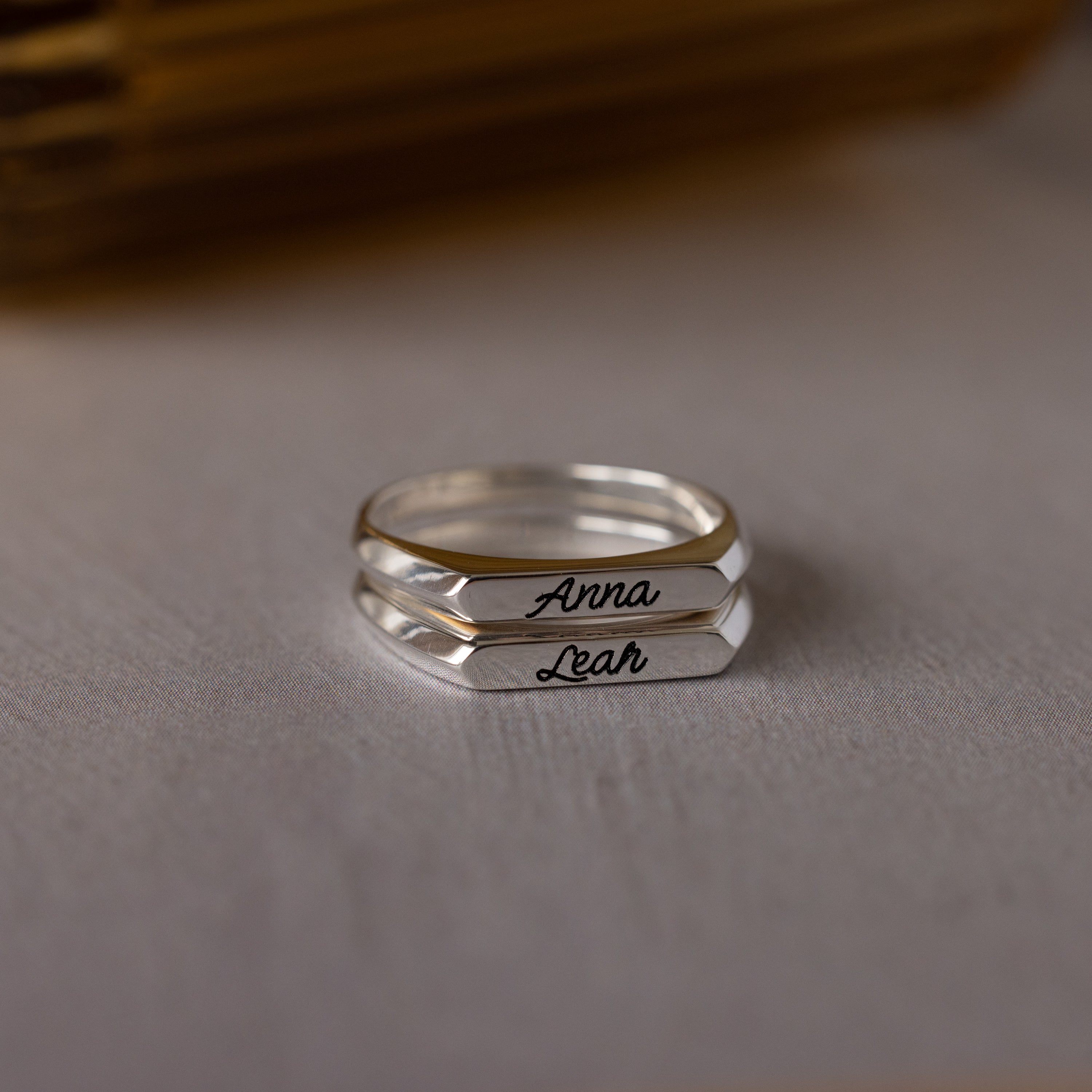 The Paris Thin Name Signet Rings in Sterling Silver, engraved with the names Anna and Leah, rest elegantly on a white surface—perfect for a personalized touch.