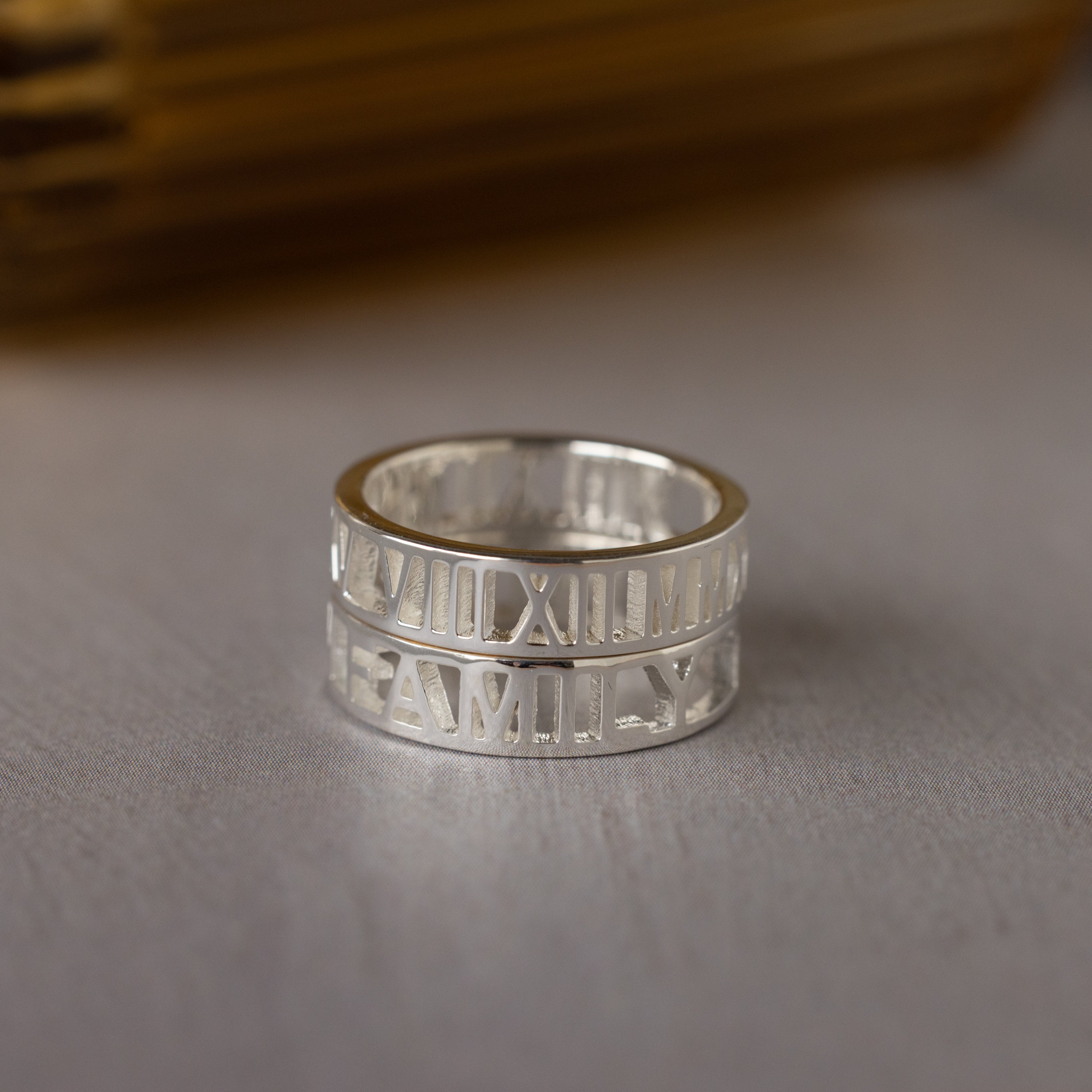 Roman Numerals Ring in Sterling Silver engraved with "FAMILY," shown on a light surface. This personalized piece combines classic style with sentiment, making it a heartfelt milestone gift.