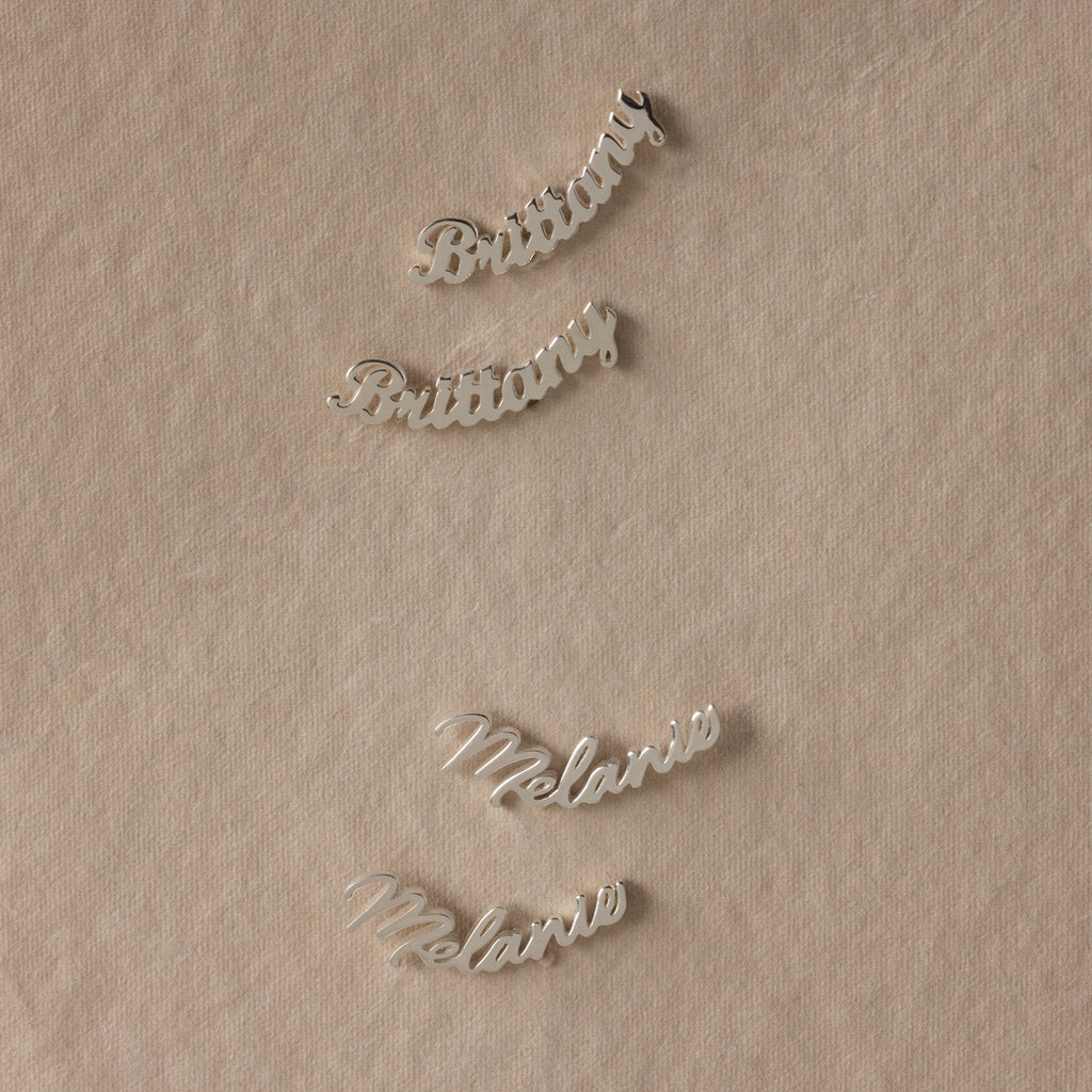 Silver nameplate earrings on a beige fabric background
