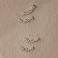 Silver nameplate earrings on a beige fabric background