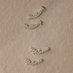 Silver nameplate earrings on a beige fabric background