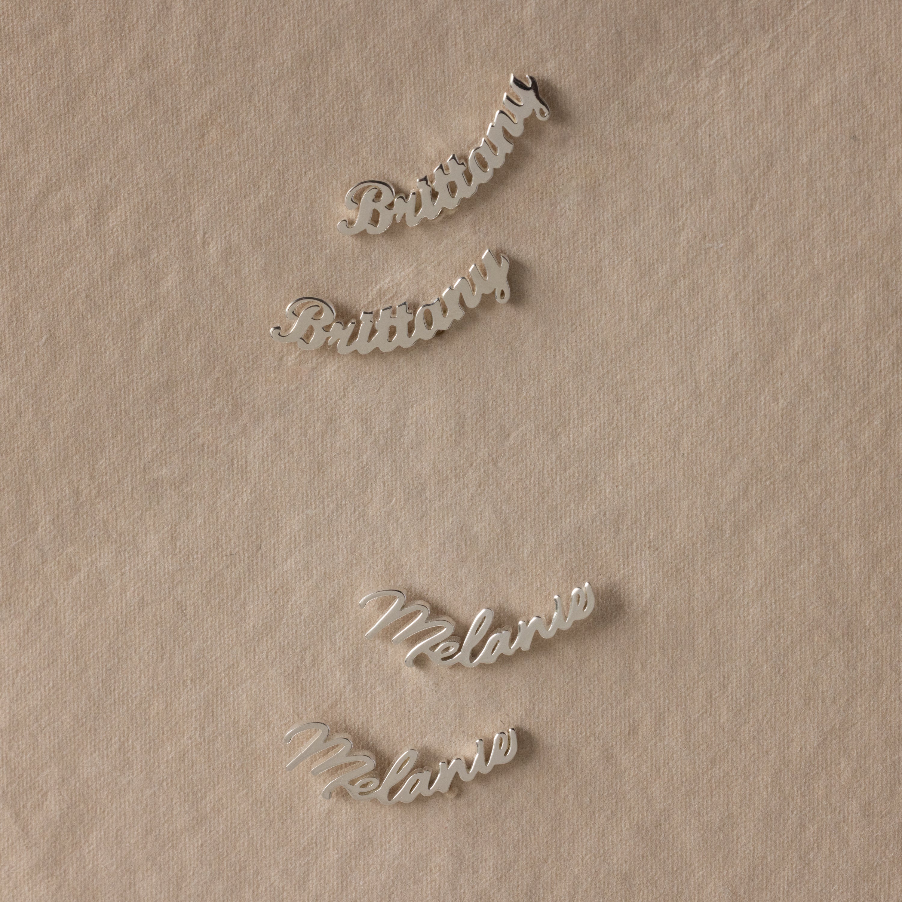 Silver nameplate earrings on a beige fabric background