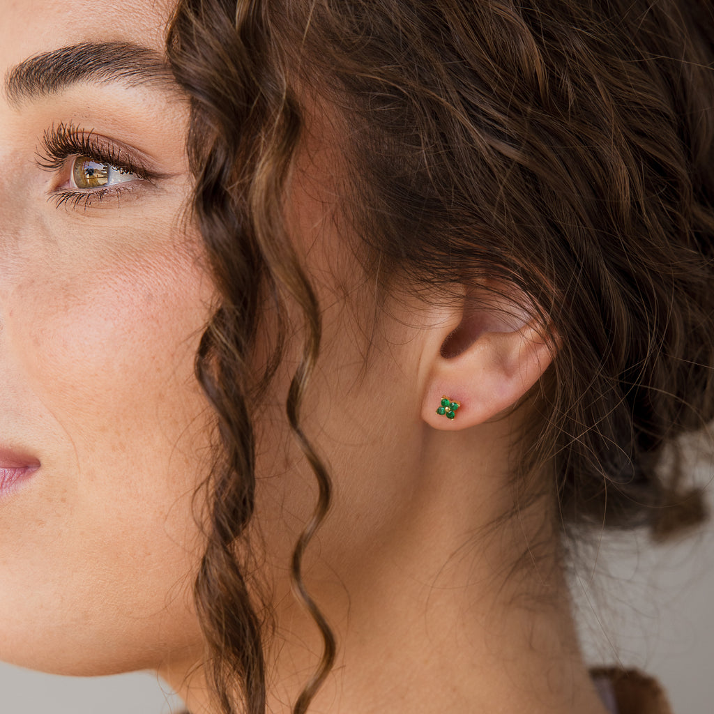 Close-up of a woman's ear wearing a small green four-leaf clover stud earring.