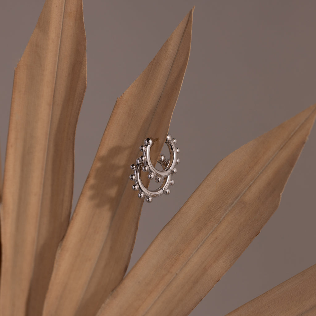 Beaded Hoops in Sterling Silver with small beads hang delicately on dried brown leaves, their textured shine standing out against a neutral background.