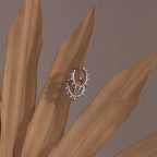 Beaded Hoops earrings, adorned with polished beads on silver hoops, are elegantly displayed on dried beige palm leaves against a muted background.