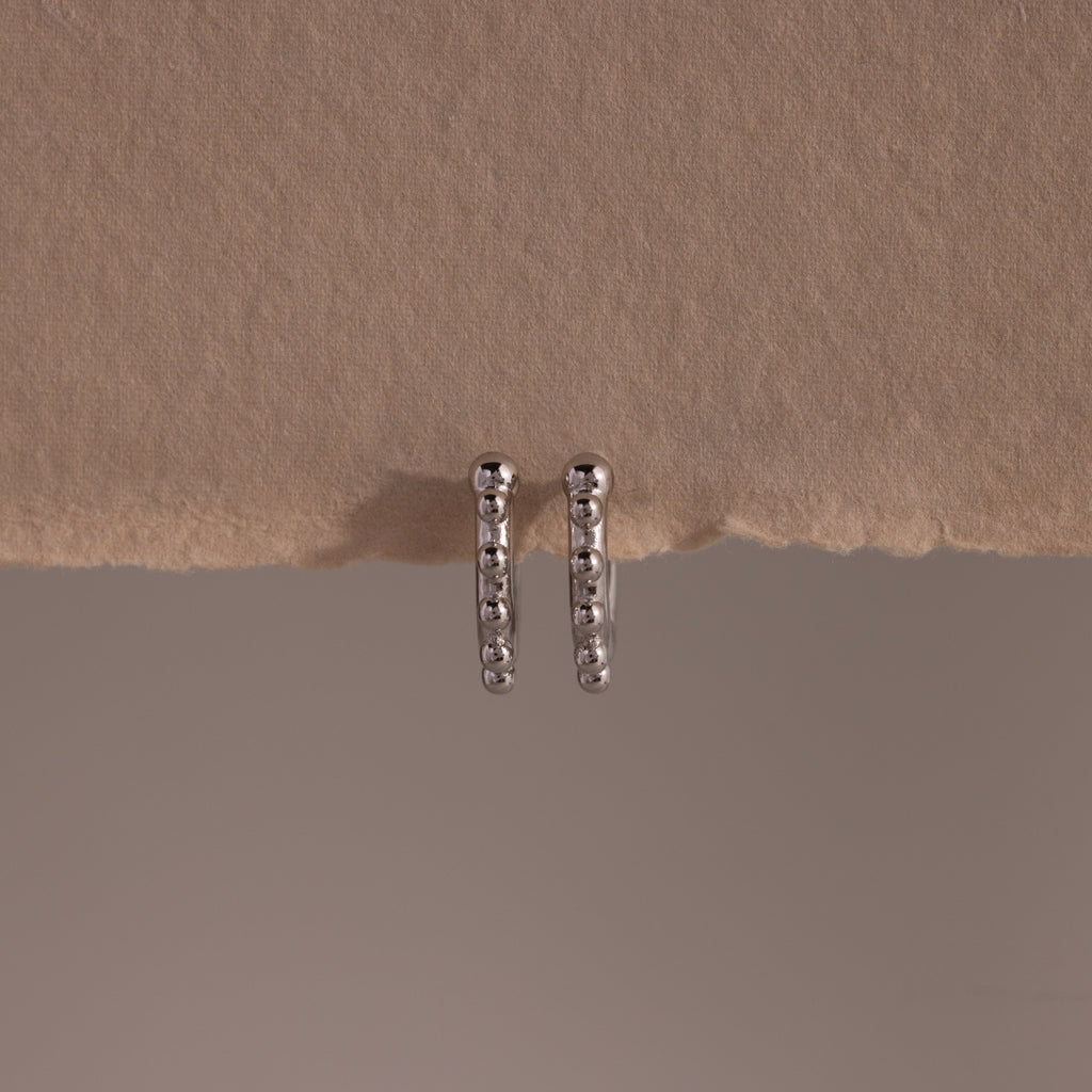 Beaded Hoops in Sterling Silver feature a beaded design that adds texture and shine, beautifully showcased against a beige textured background.