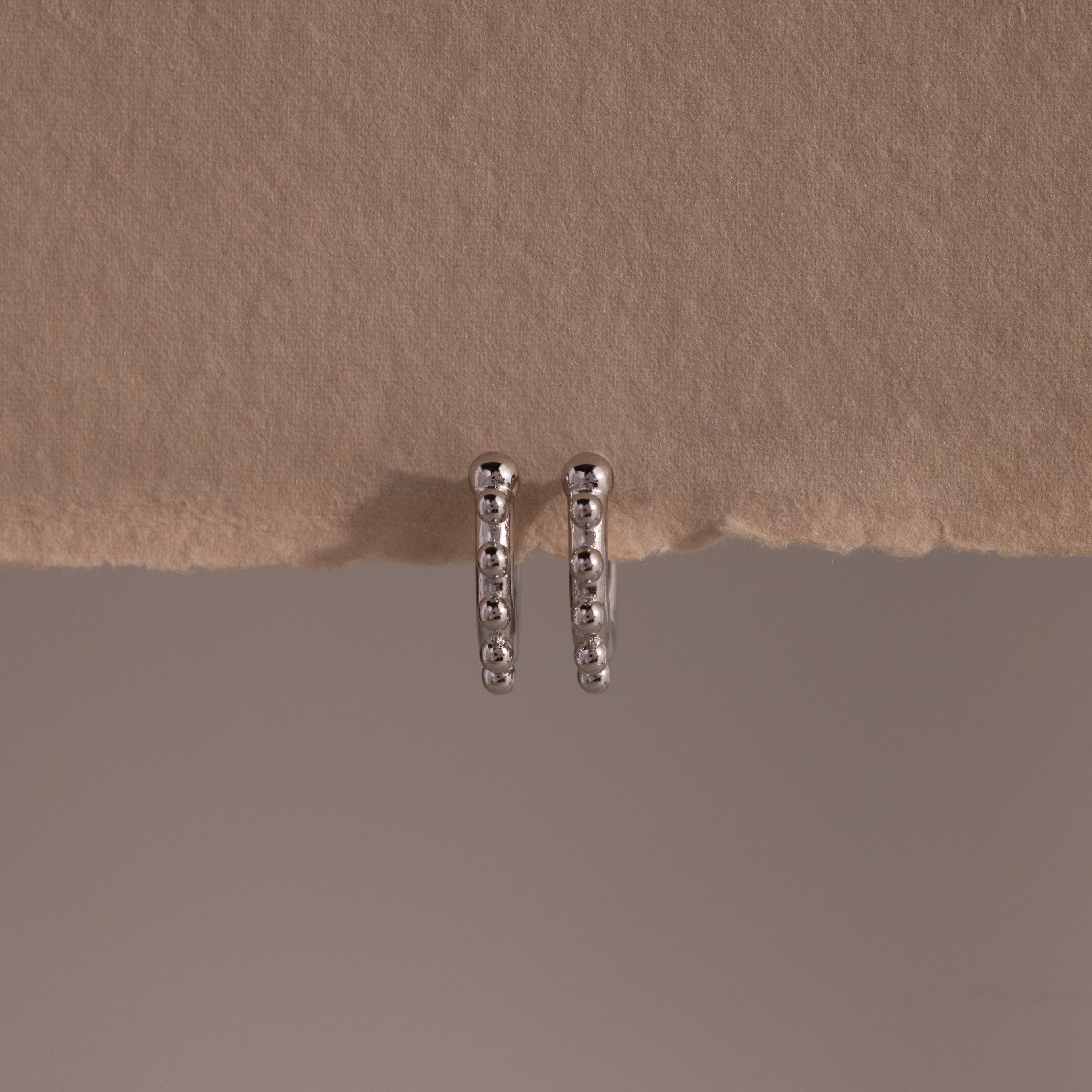 Beaded Hoops in Sterling Silver feature a beaded design that adds texture and shine, beautifully showcased against a beige textured background.