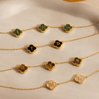 Five gold chain bracelets with flower-shaped letter pendants display H, E, A, T, D, S, Y, M, and L on a beige surface—ideal for stacking or pairing with the Gemstone Clover Letter Necklace.