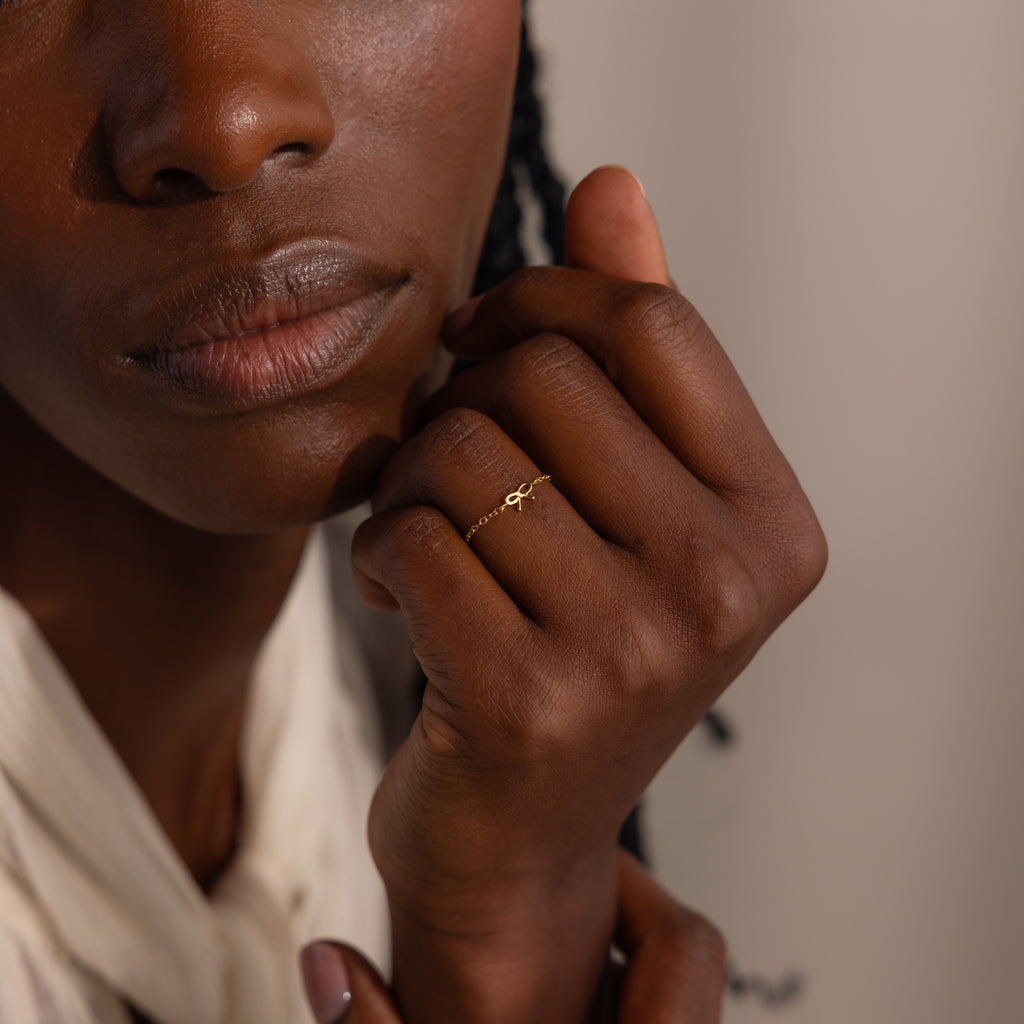Close-up of model gently resting her hand near her face, showcasing a dainty gold chain ring with a petite bow design.