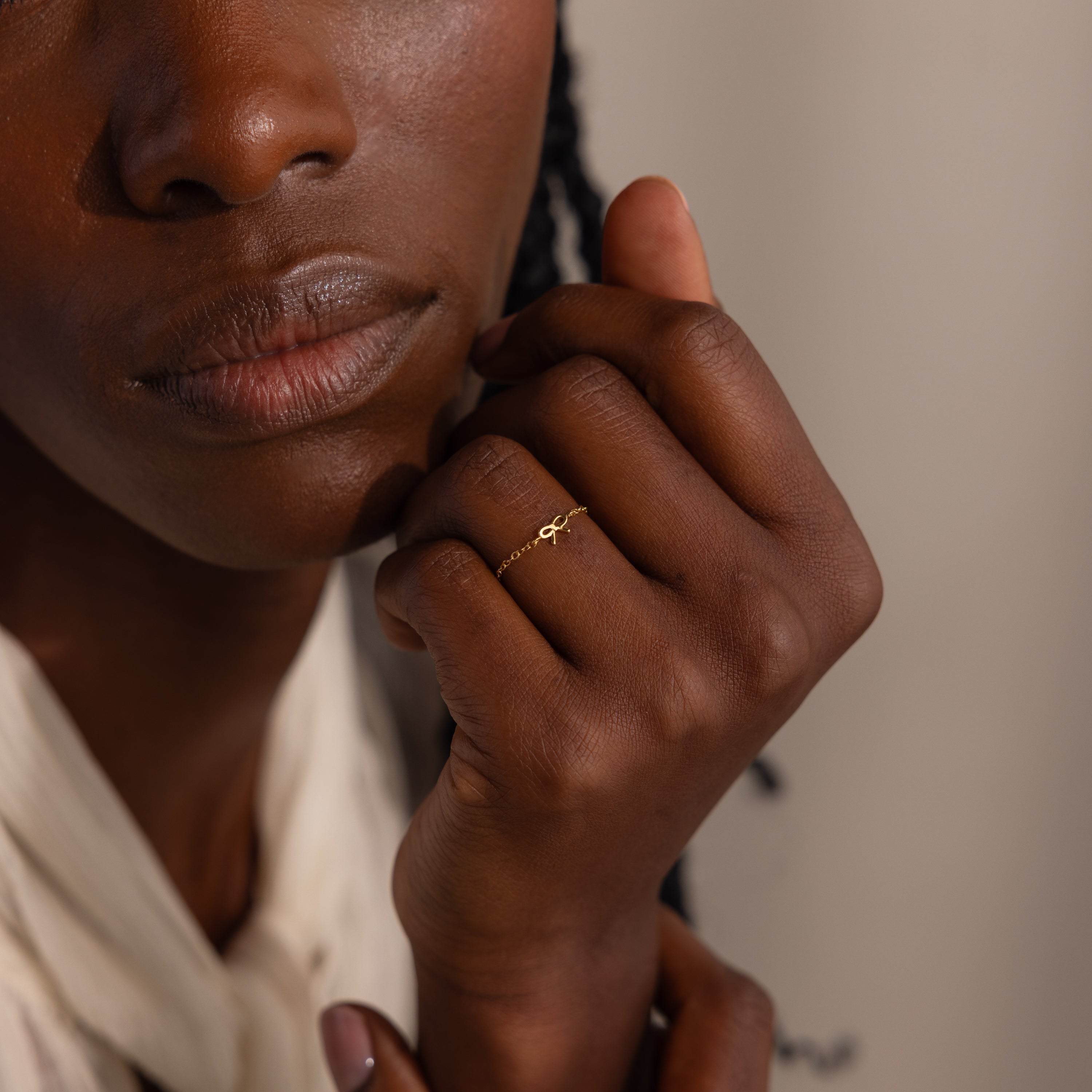 Close-up of model gently resting her hand near her face, showcasing a dainty gold chain ring with a petite bow design.