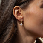 Close-up of a womans ear wearing Pearl Diamond Drop Earrings, vintage-inspired with a gold setting, pearl drop, and floral detail.