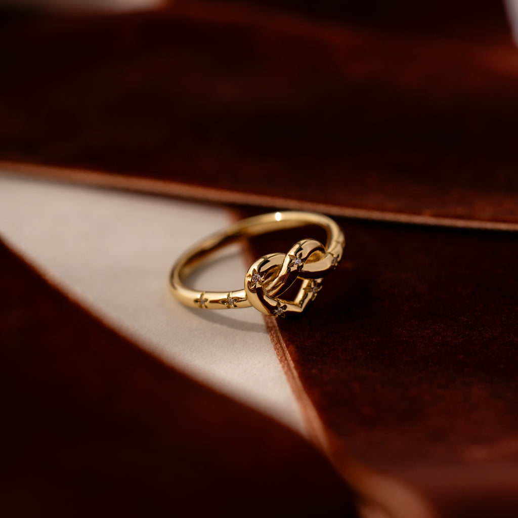 The Starry Love Knot Ring, featuring a decorative gold design, is displayed on a soft brown velvet surface.