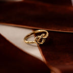 The Starry Love Knot Ring, featuring a decorative gold design, is displayed on a soft brown velvet surface.