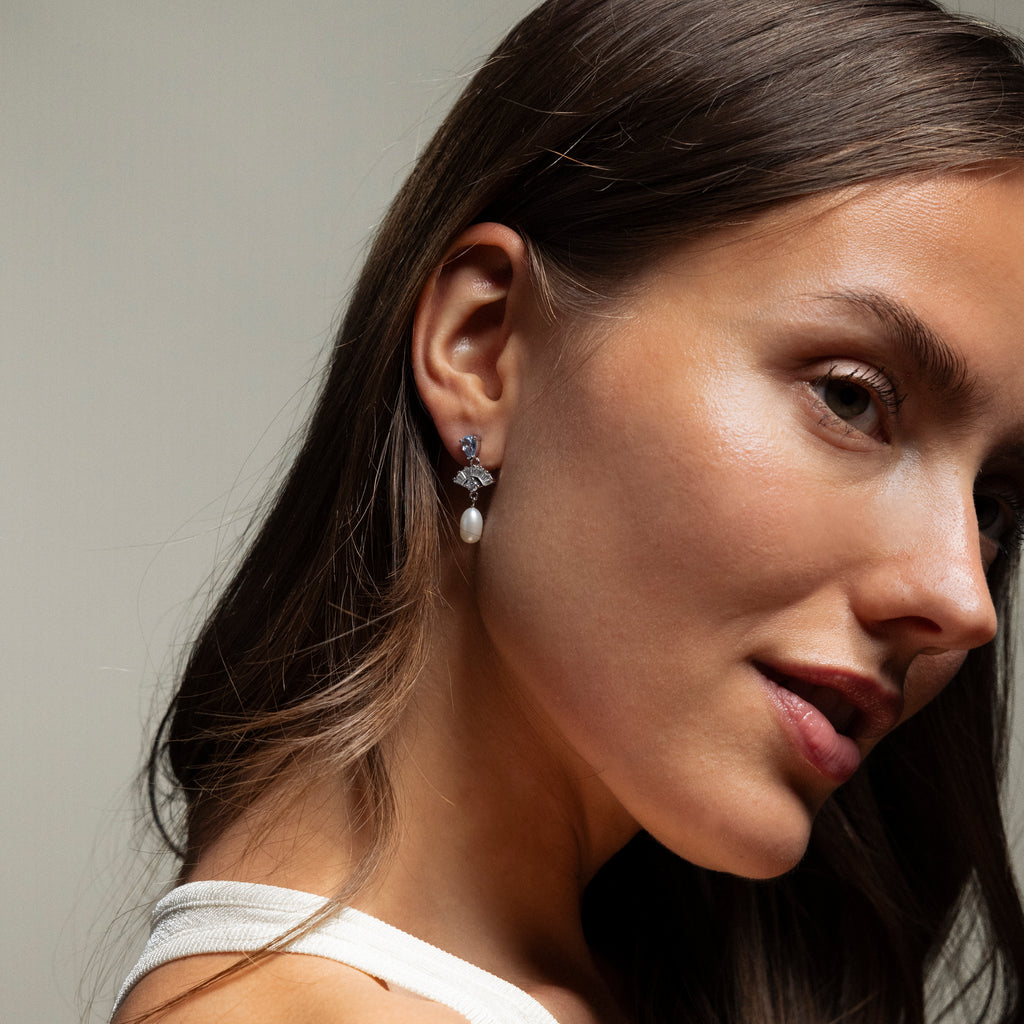 A woman in a white top showcases Aquamarine Pearl Drop Earrings, radiating vintage glamour as she glances over her shoulder against a neutral background.