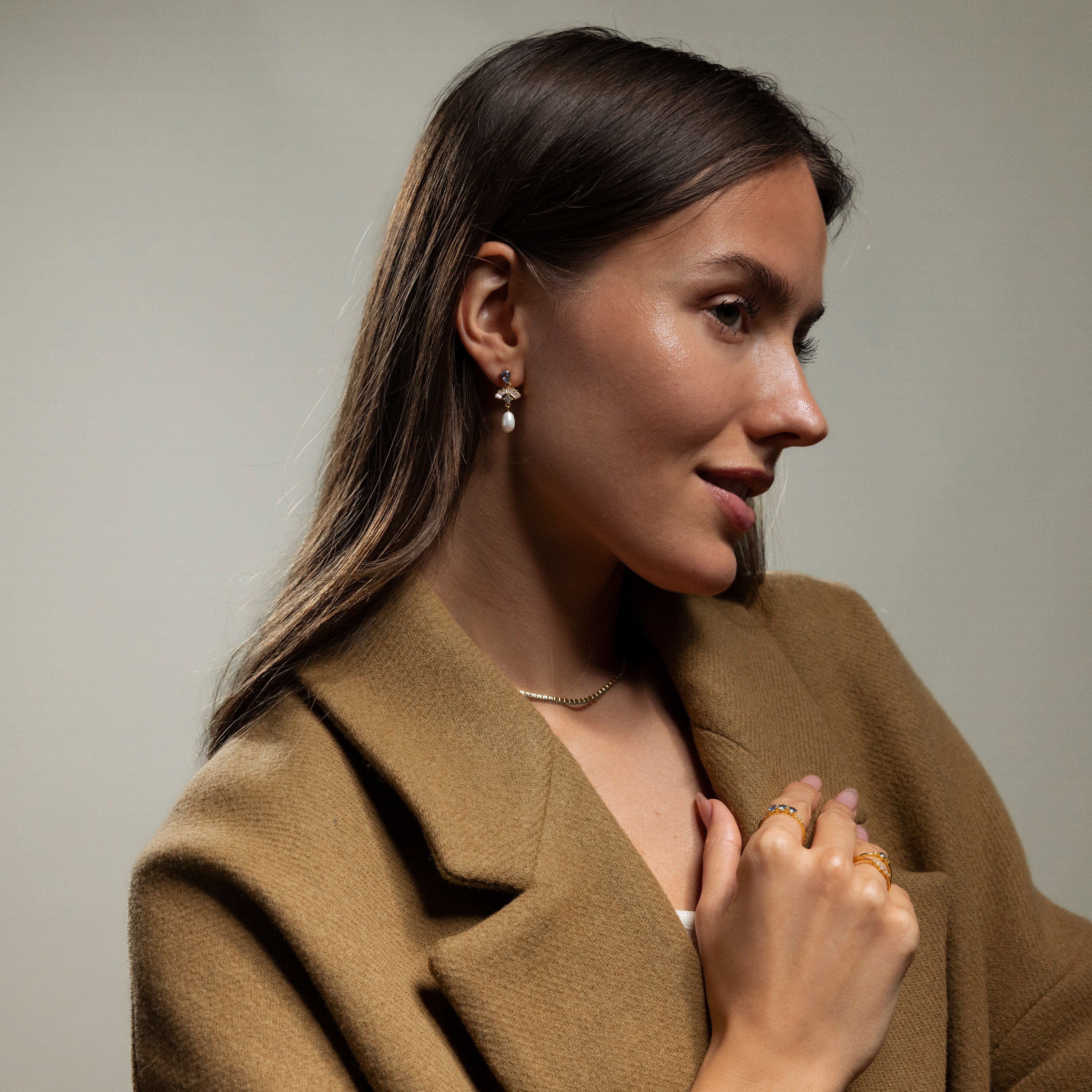 Woman in a tan coat wears Aquamarine Pearl Drop Earrings and gold jewelry, exuding vintage glamour as she looks to the side against a neutral background.