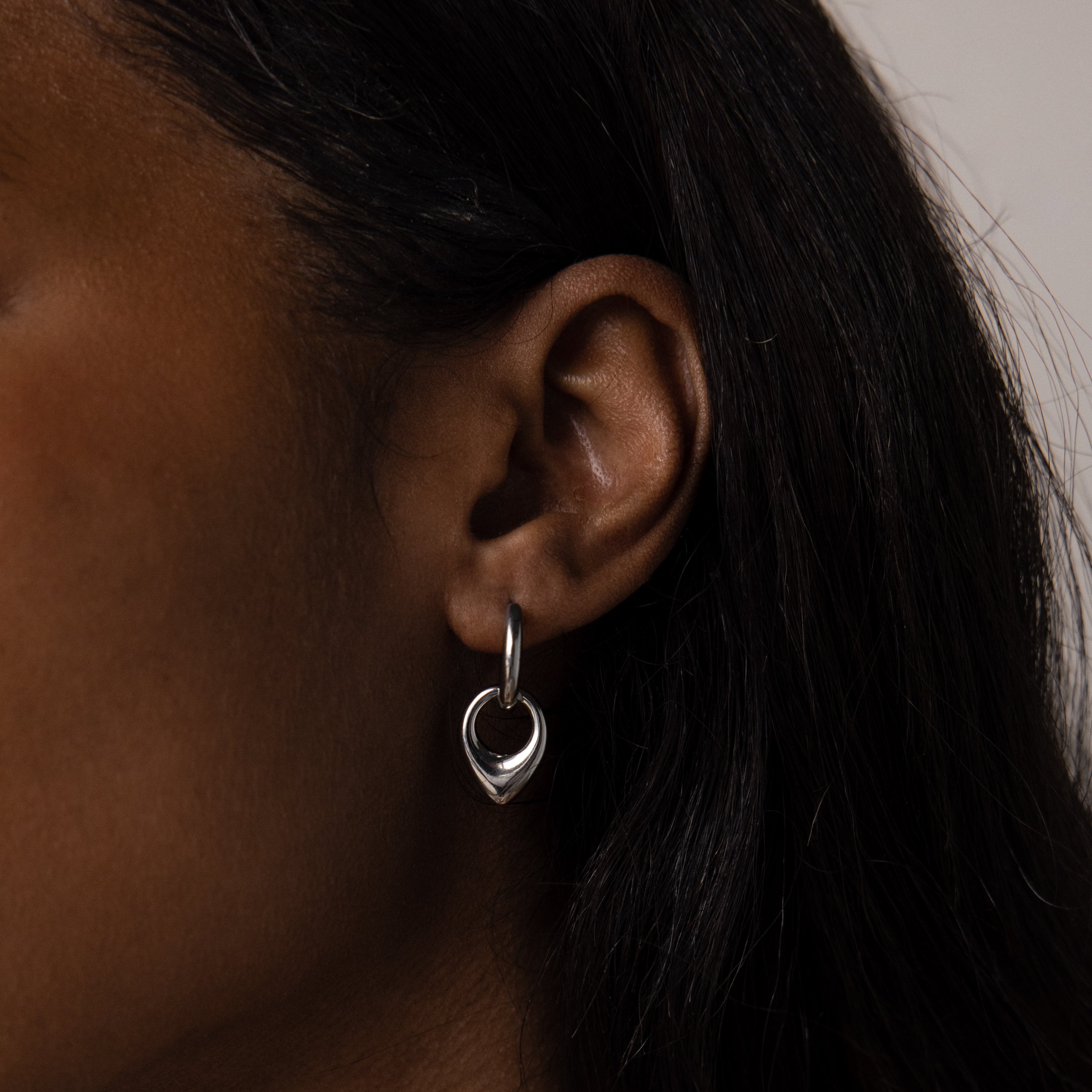 Close-up of a person’s ear wearing Bold Teardrop Hoops, showcasing the timeless appeal and versatility of these silver earrings against a neutral background.