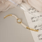 The Pearl Link Timepiece with diamond accents sits on sheet music next to a tilted champagne glass and beige fabric, radiating vintage elegance.