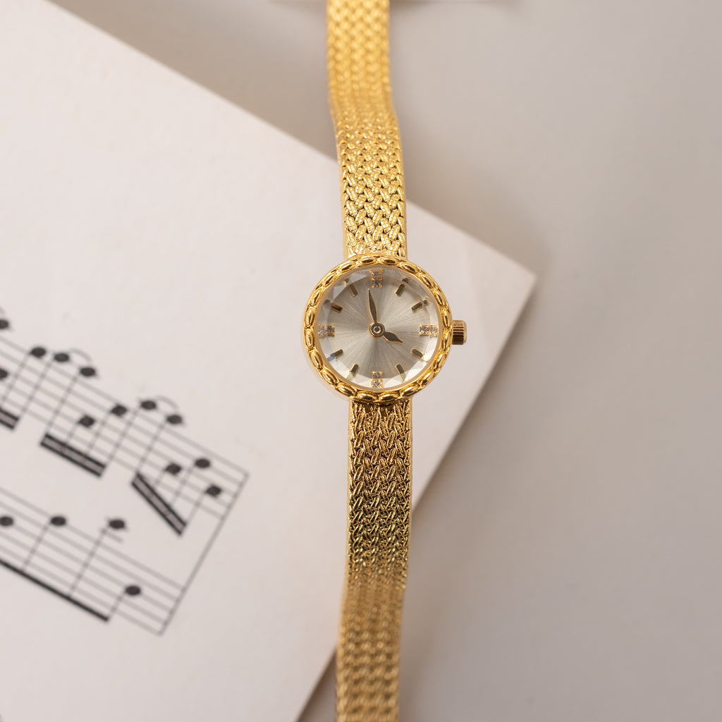Top-down view of the gold round braided watch laid across a page with sheet music.
