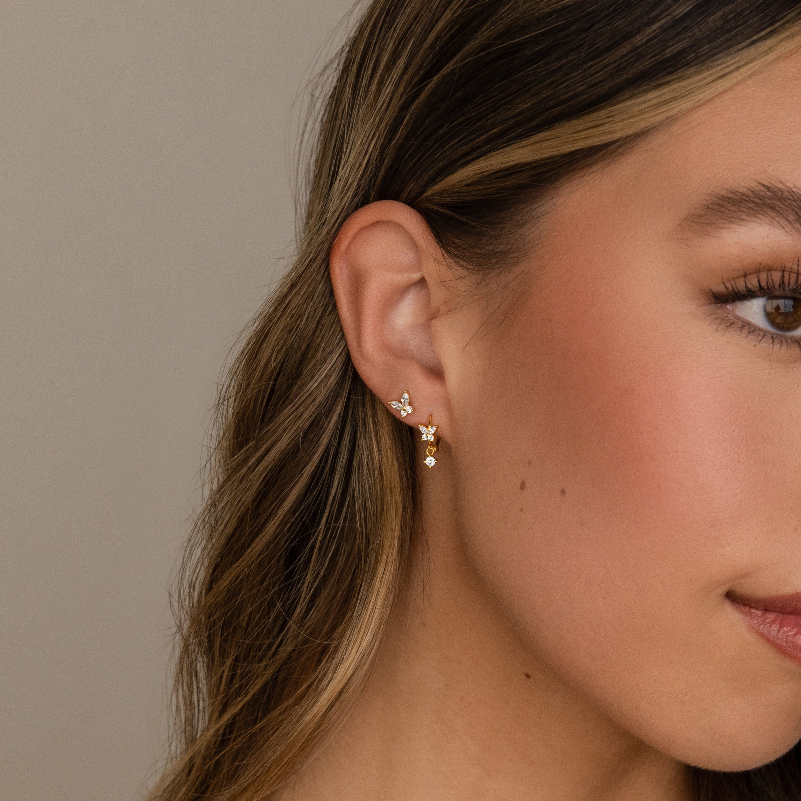 Close-up of a woman's ear adorned with two Butterfly Drop Huggies in 18K Gold, her brown hair tucked behind her ear.