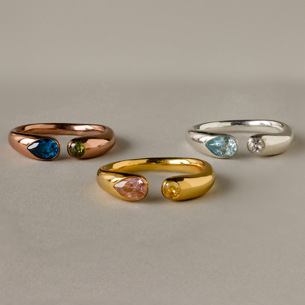 The Toi et Moi Birthstone Signet Ring features three metal bands—rose, gold, and silver—each set with two teardrop-shaped gemstones, displayed beautifully on a light background.
