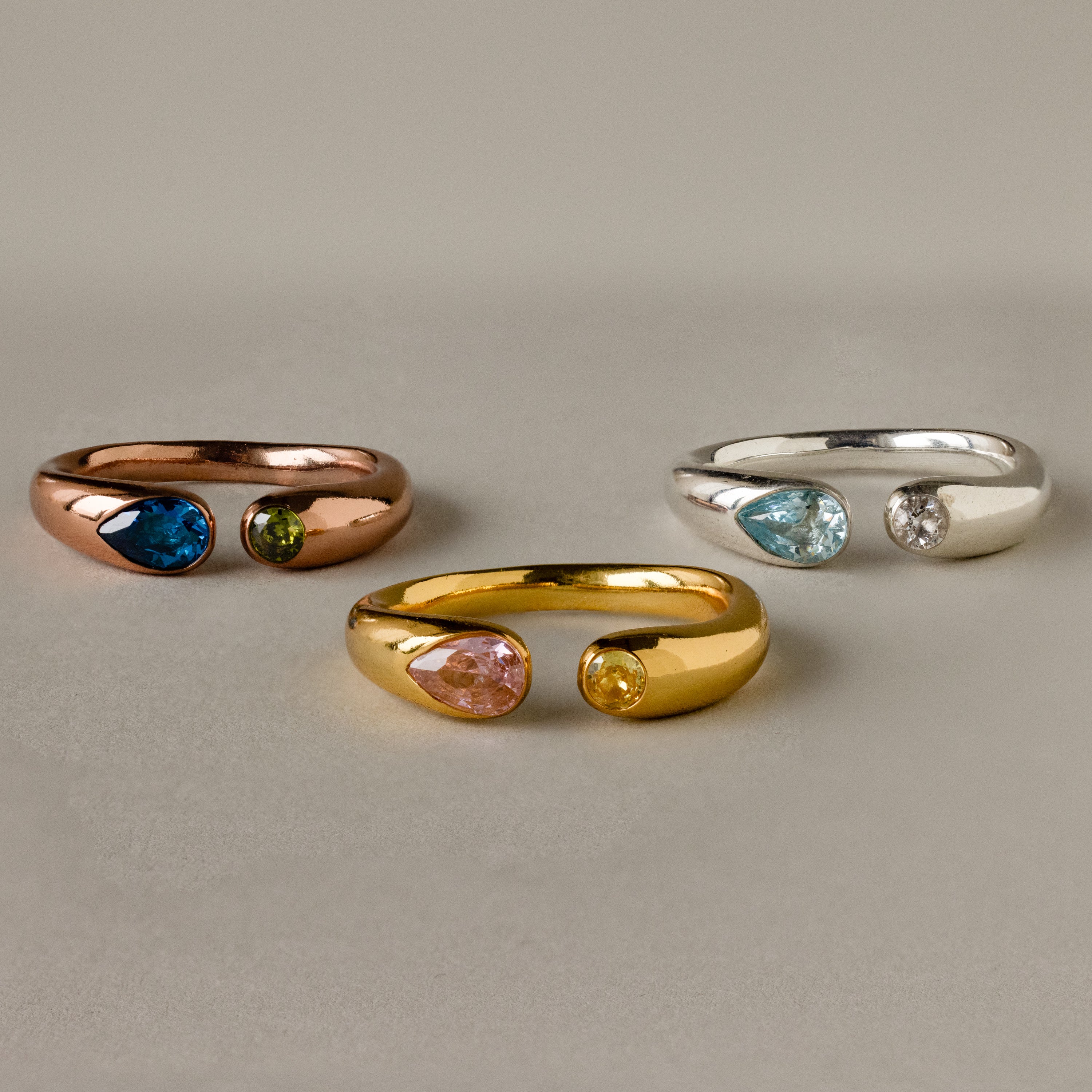 The Toi et Moi Birthstone Signet Ring features three metal bands—rose, gold, and silver—each set with two teardrop-shaped gemstones, displayed beautifully on a light background.