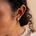 A close-up shows a person wearing Pave Checkered Huggies, with curly hair partly visible.