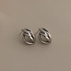 The Bold Multi Knot Studs in silver feature an intricate knot design, embodying modern elegance against a light beige background.