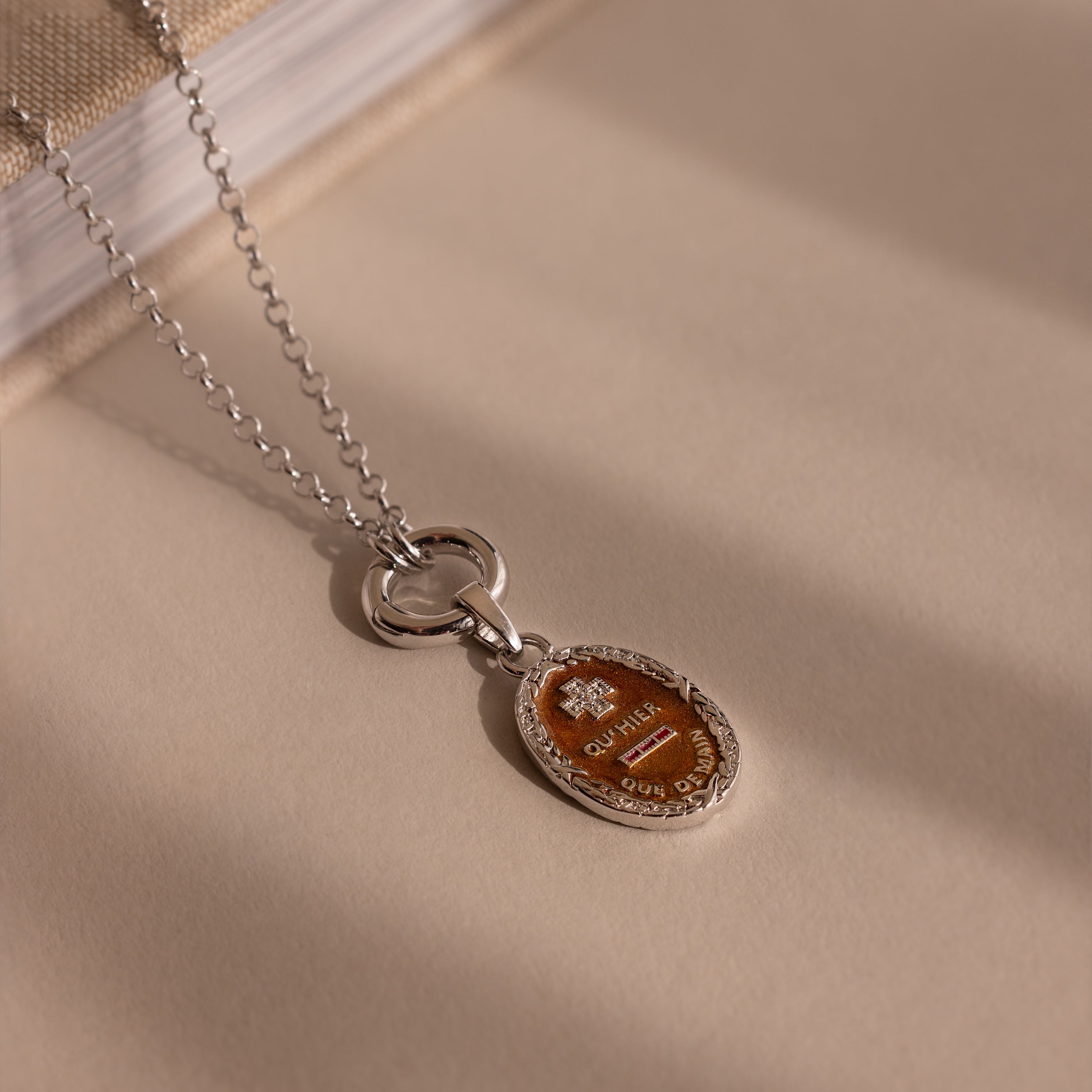 The Love Poem Pendant Necklace, featuring a silver chain and oval brown pendant, rests on a beige surface beside a book—a subtle token of love.