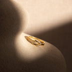 The Pave Double Knot Ring rests on a smooth, beige, curved surface in soft light.