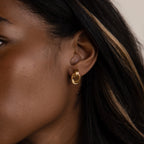 Close-up of a womans ear with dark hair and a light streak, wearing Micro Triple Knot Earrings in 18K Gold, embodying quiet luxury.