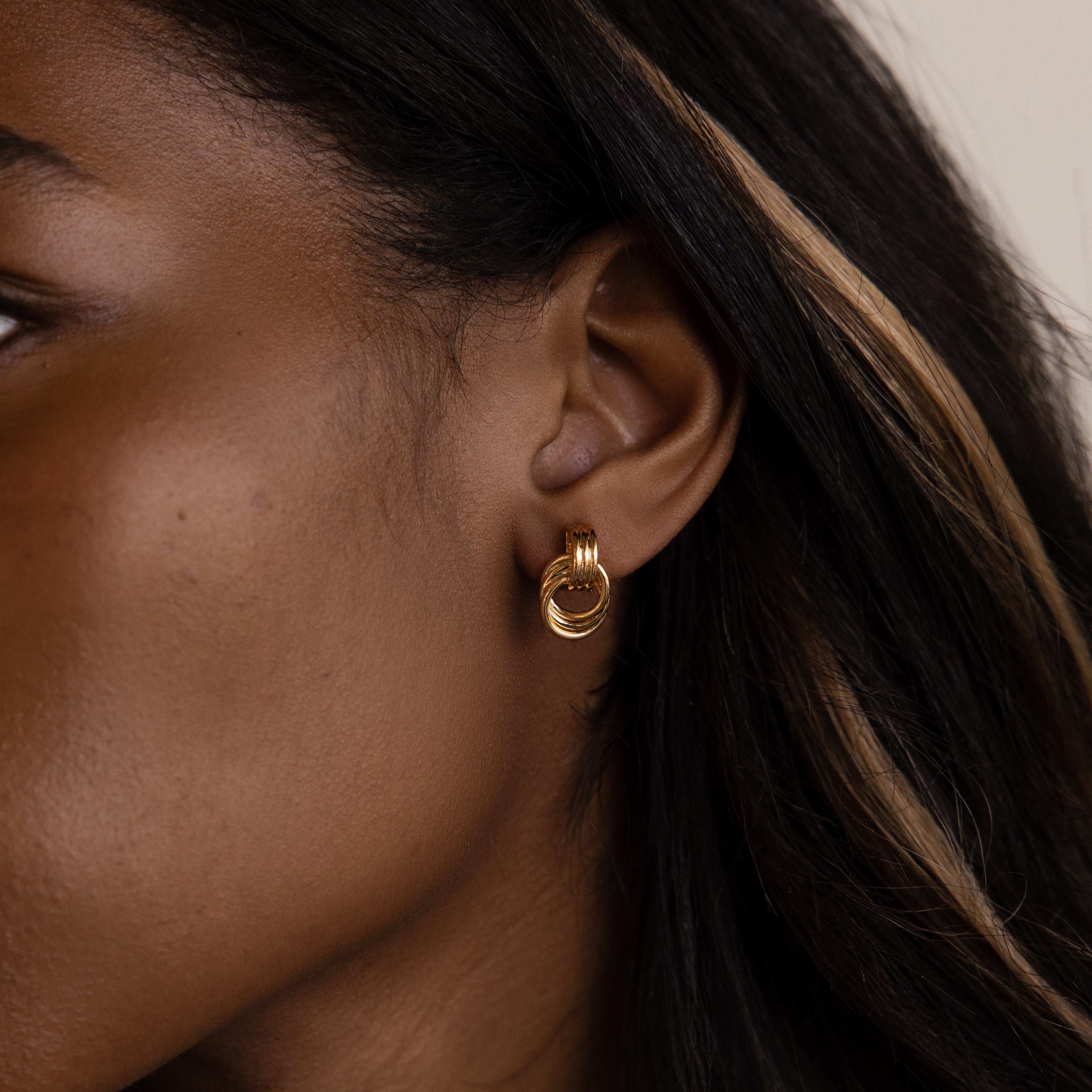 Close-up of a woman with dark hair and a blonde streak wearing Micro Triple Knot Earrings and layered gold hoops for an effortless quiet luxury look.