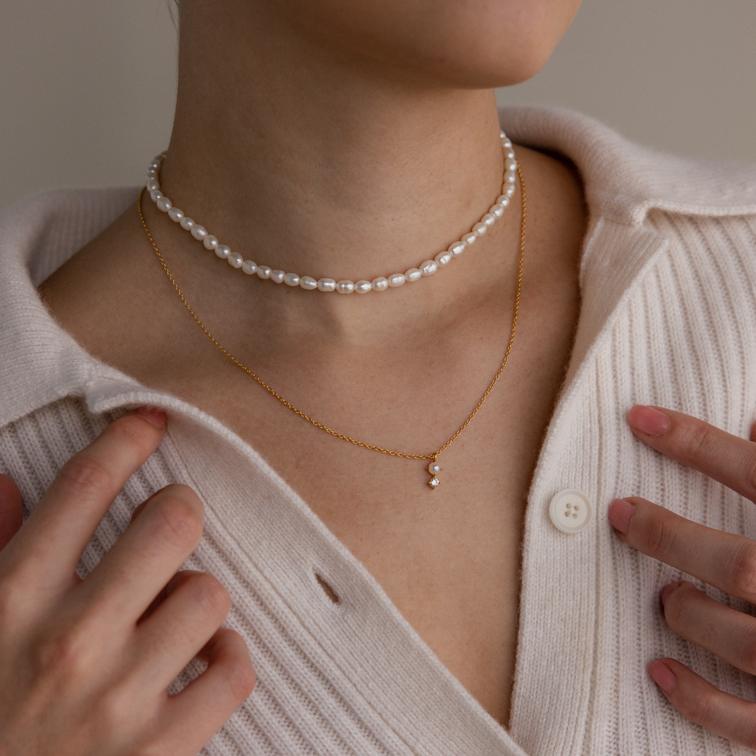Close-up of a person wearing the Pearl Diamond Drop Necklace over a cream ribbed sweater.