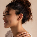 Model wearing a tiny 6mm gold huggie hoop earring on her upper ear cartilage, styled with a soft neutral backdrop.