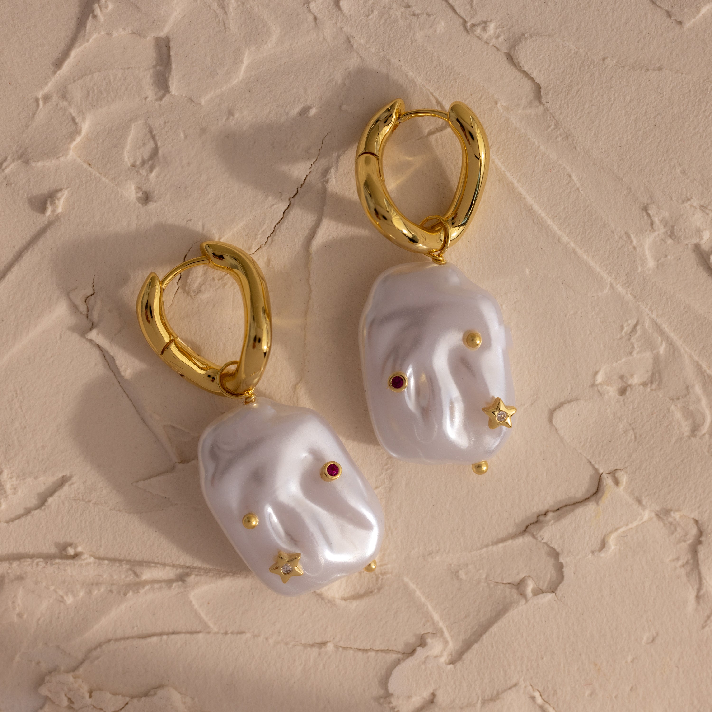 Celestial Baroque Pearl Charm Hoops in 18K Gold showcase irregular white pearls on gold hoops, accented with delicate gold, red, and star charms for a unique celestial-inspired look.