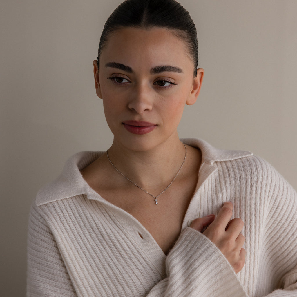 Woman in a cream ribbed sweater wearing the Pearl Diamond Drop Necklace in Silver, looking to the side against a neutral background.