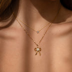 Two gold necklaces grace her neck: one with a delicate gem pendant, and the other a coquette-inspired accessory featuring the Diamond Bow Charm in 18K Gold, sparkling with CZ diamonds.