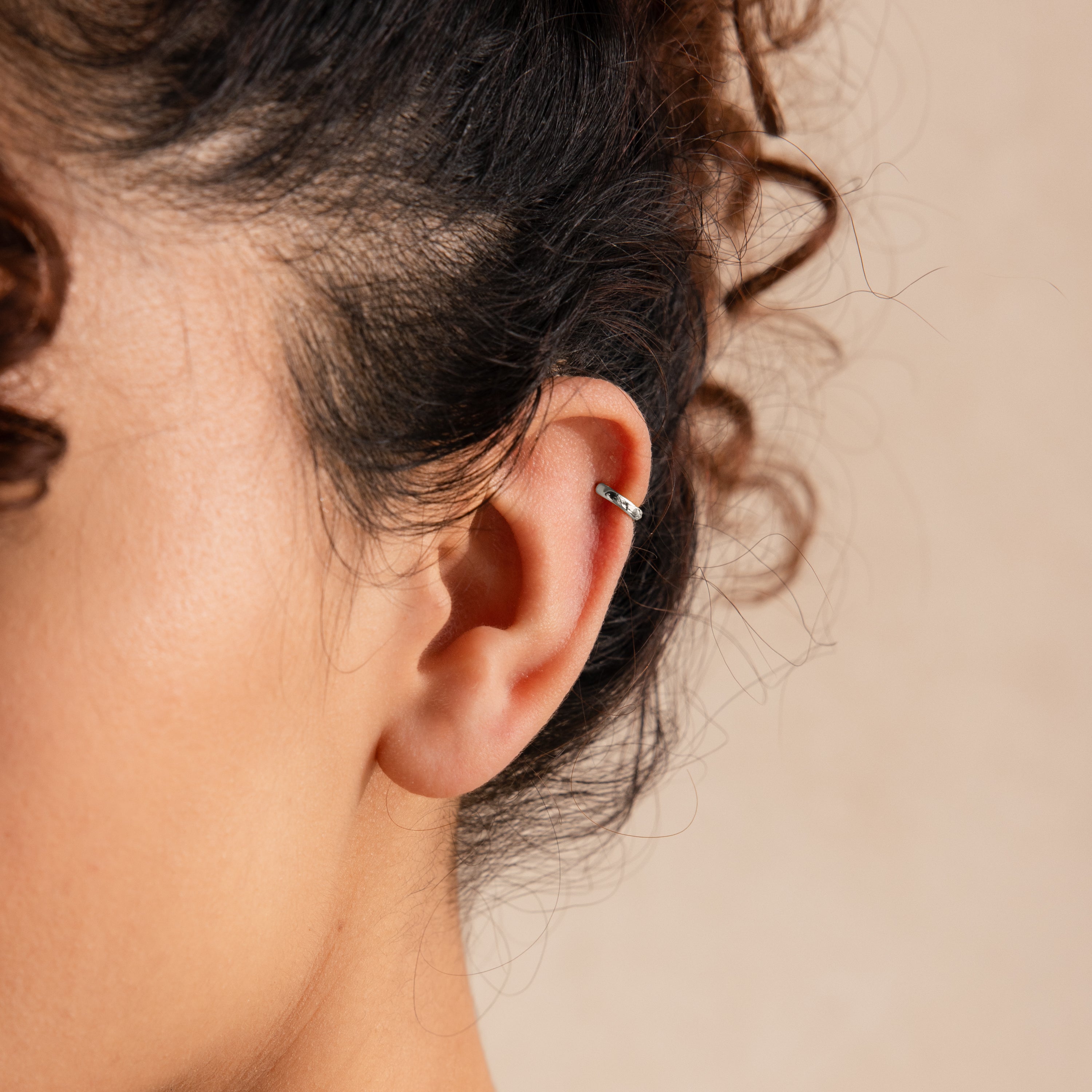 Close-up of a 6mm tiny classic silver huggie hoop earring worn on the upper ear cartilage.