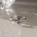 Silver ring with a green agate baguette-cut gemstone on a reflective surface